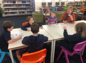 Teacher holding up a word card sitting at a table with five students playing bingo