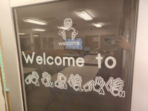Classroom door sign reading “Welcome to Auslan,” with illustrated hand signs spelling out the word Auslan.