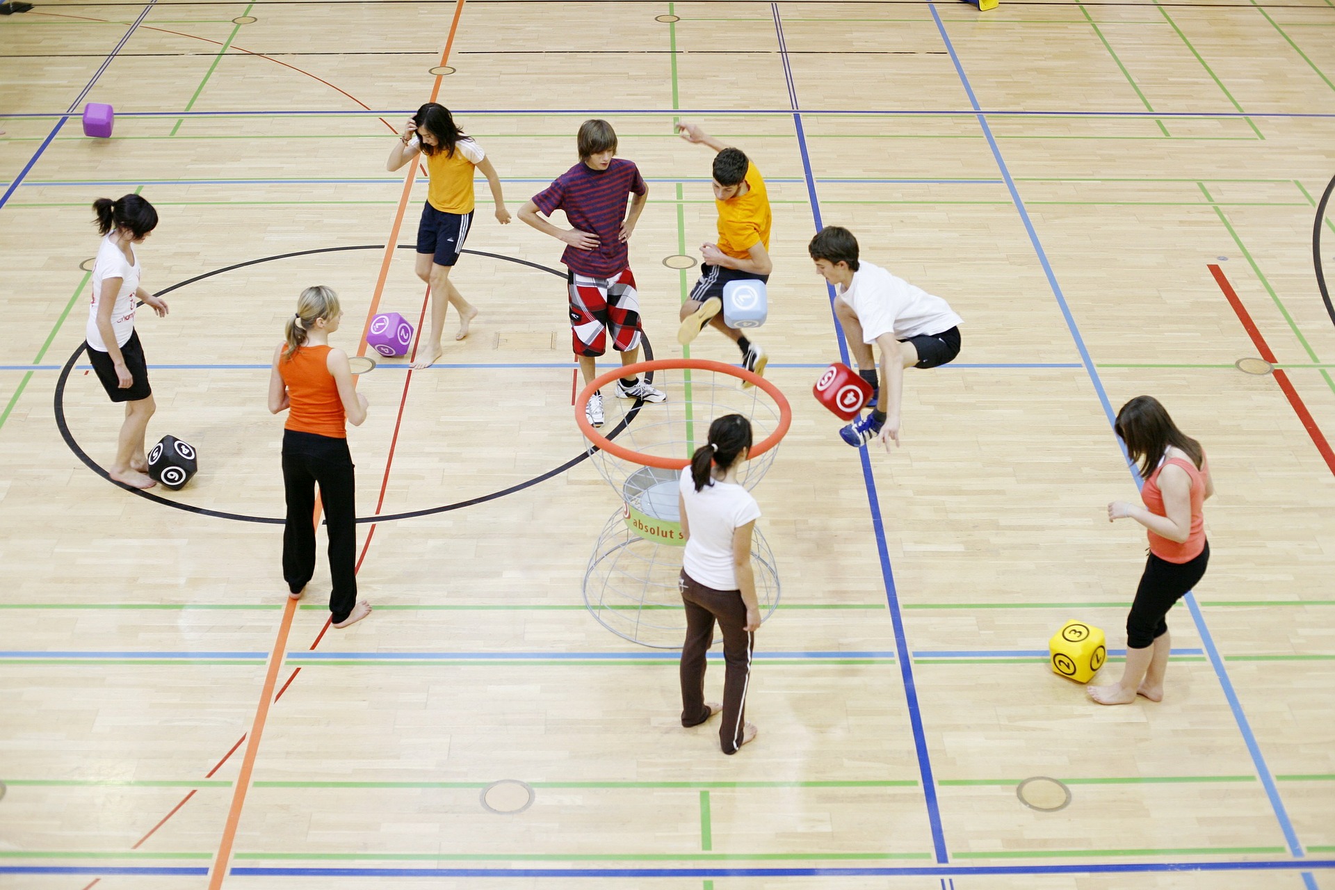 8 kids playing with cubed-shaped balls in a school gym.